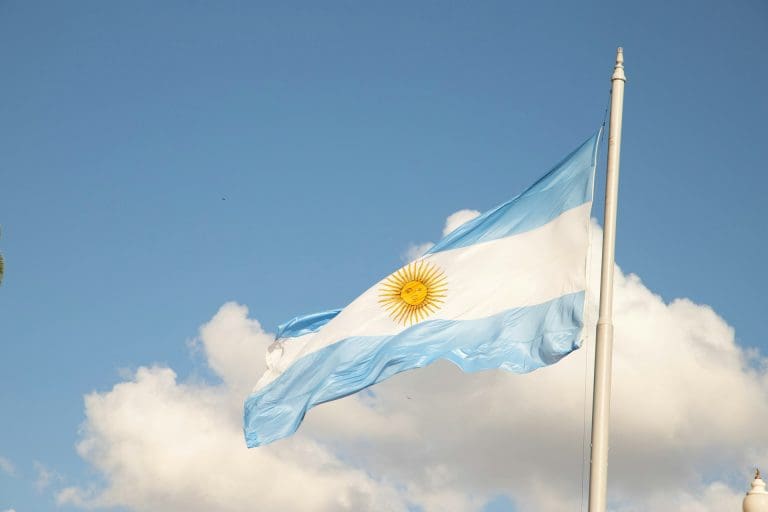 Argentiniens Inflationsrate ein Problem? — Foto von <a href="https://unsplash.com/de/@gustavo0351?utm_content=creditCopyText&utm_medium=referral&utm_source=unsplash">Gustavo Sánchez</a> auf <a href="https://unsplash.com/de/fotos/eine-flagge-die-im-wind-weht-mit-einem-glockenturm-im-hintergrund-yhhVap-uWvo?utm_content=creditCopyText&utm_medium=referral&utm_source=unsplash">Unsplash</a>